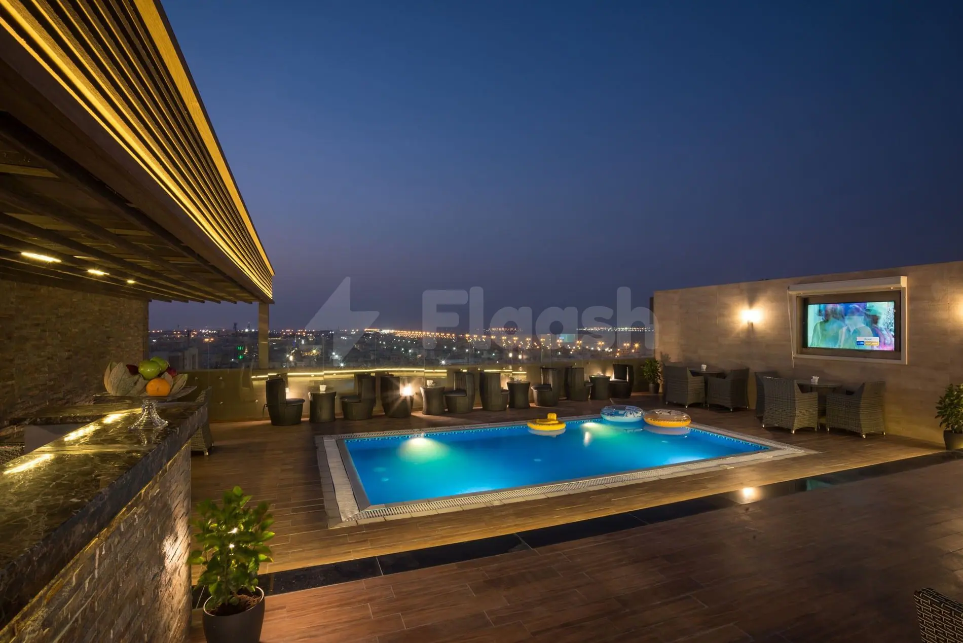 Rooftop terrace at Naviti By Warwick Dammam in Dammam with illuminated rectangular pool and city skyline view