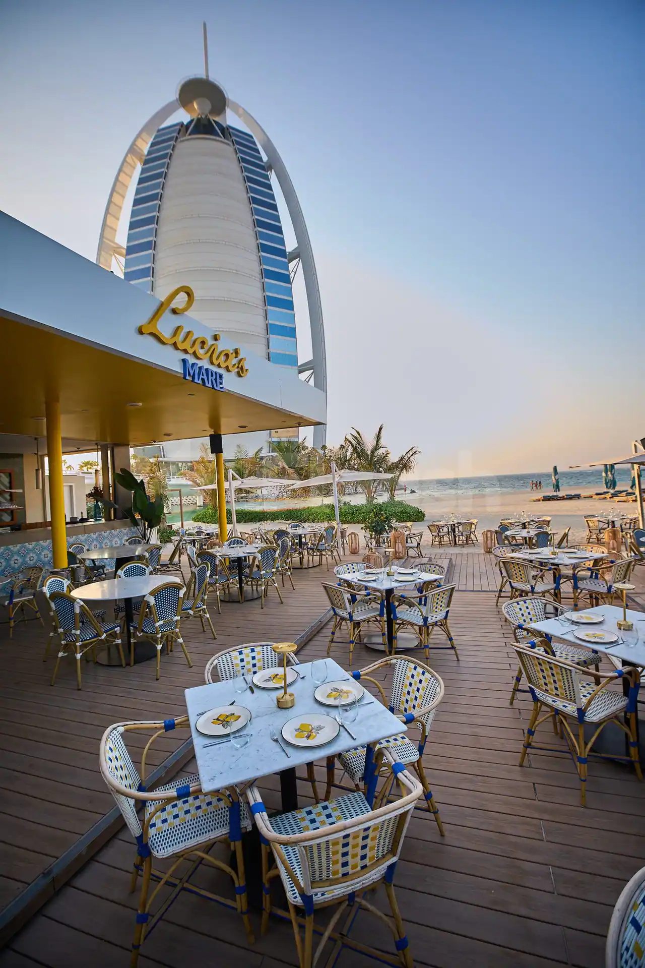 Terrace at Lucia's Mare Restaurant Dubai with wooden deck, patterned wicker chairs, marble tables, and Burj Al Arab