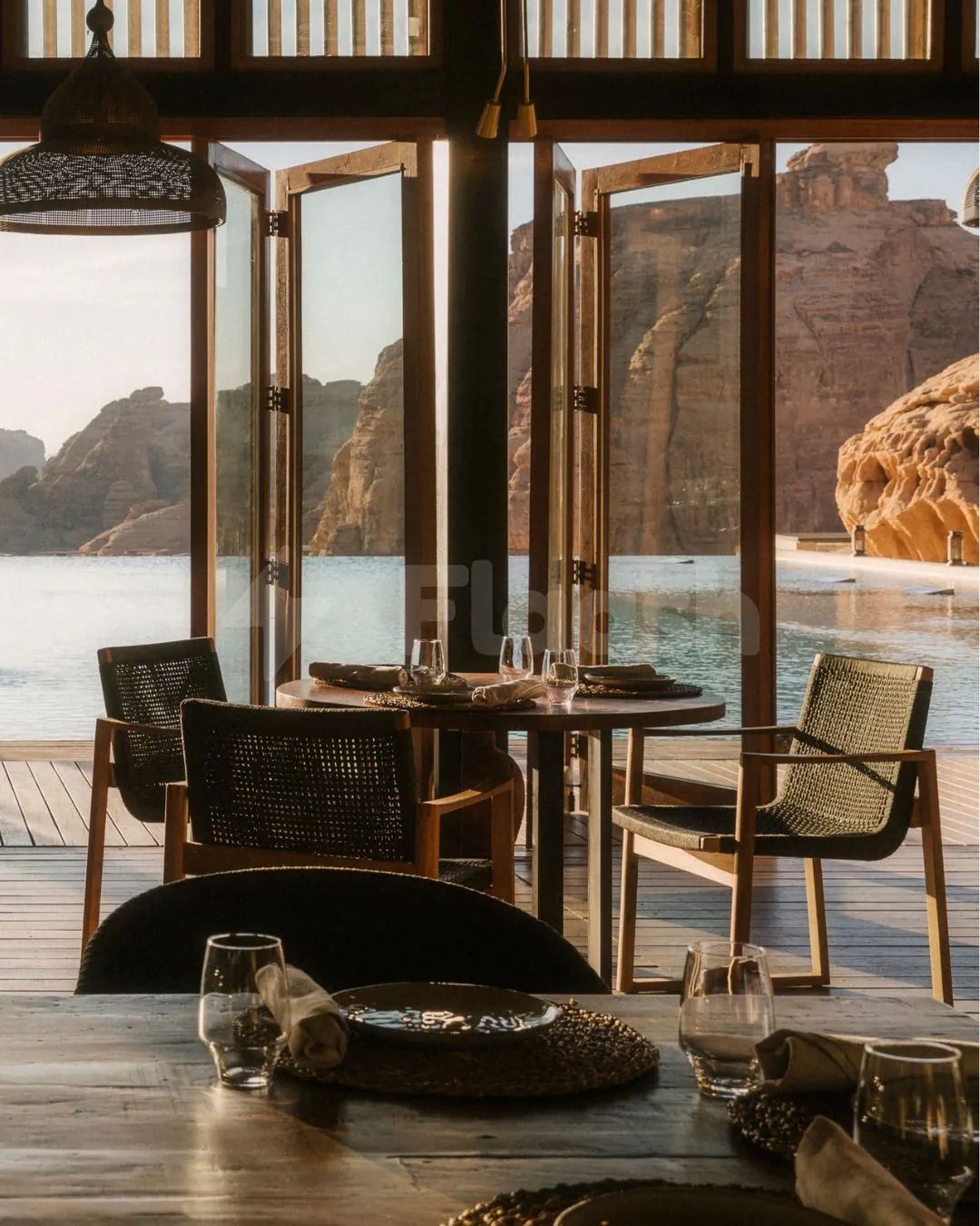 Restaurant at Tama At Habitas AlUla with round wooden table, woven chairs, and open glass doors framing desert