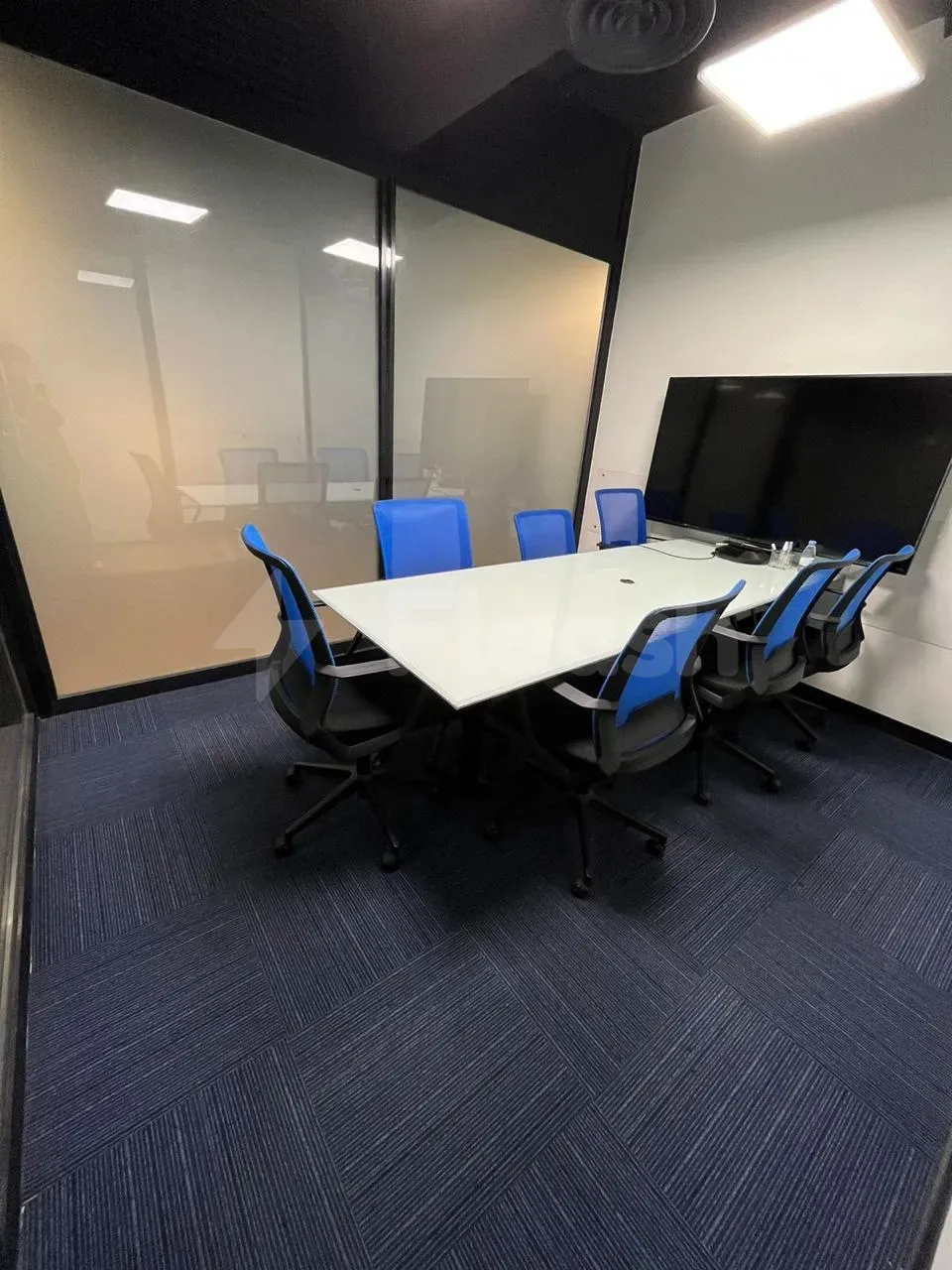 Boardroom at Basix Coworking Space Jeddah featuring a white rectangular table, blue-black ergonomic chairs, and a frosted glass