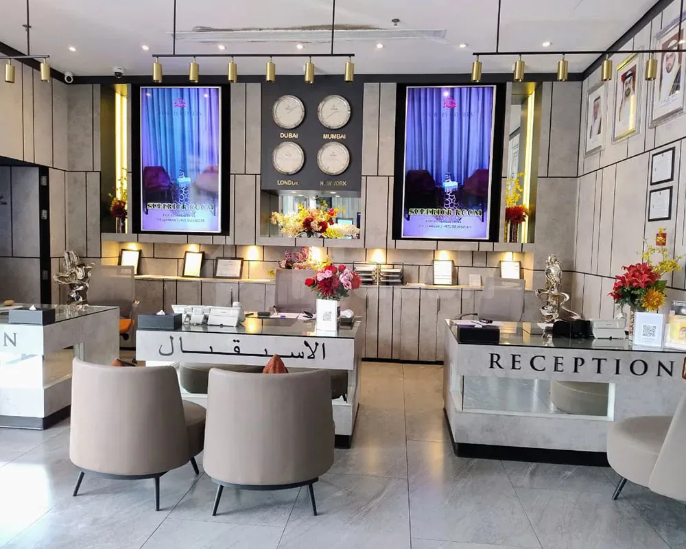 Reception desk at Fortis Hotel Fujairah featuring glass countertops, white marble bases, and digital screens displaying city time
