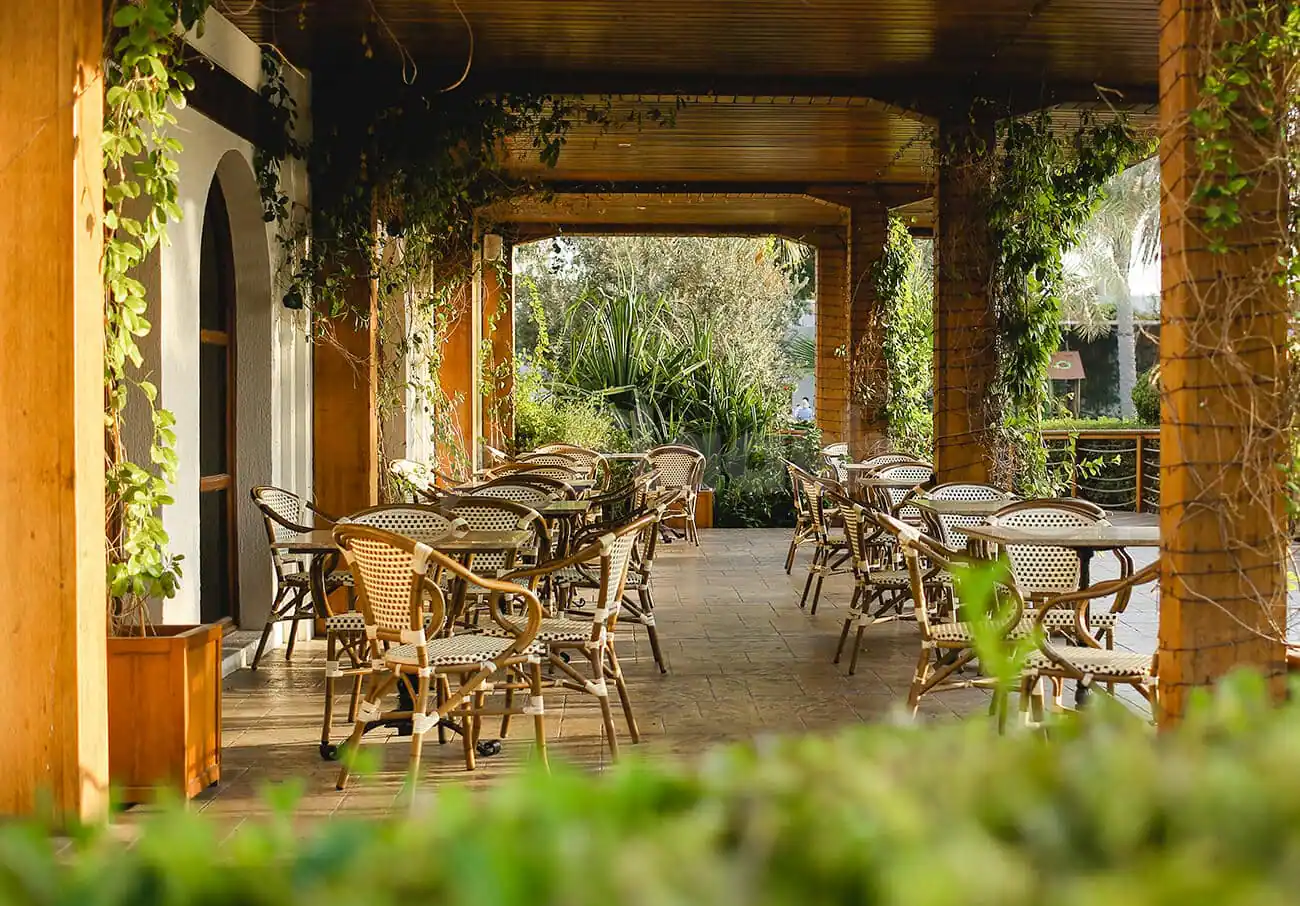 Covered outdoor terrace at Flooka Restaurant Dubai featuring wooden beams, climbing ivy, and arched doorways opening to lush