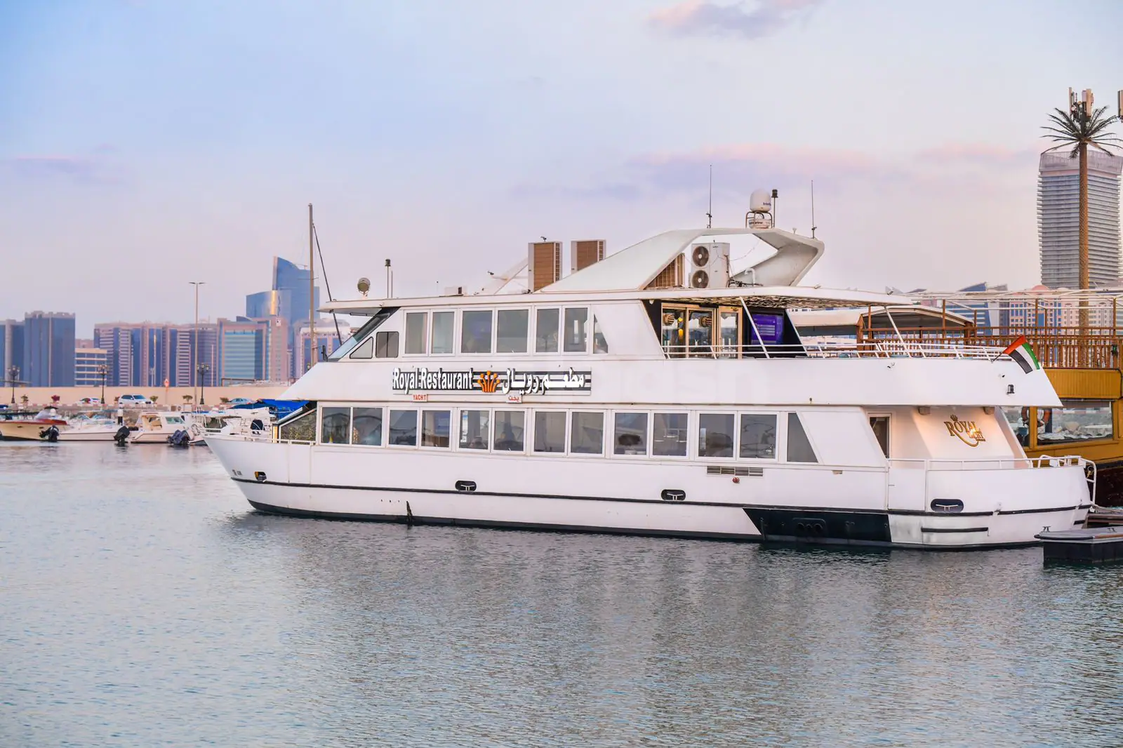 White multi-level Royal Yacht Restaurant vessel docked in Abu Dhabi marina with large windows and glass railing