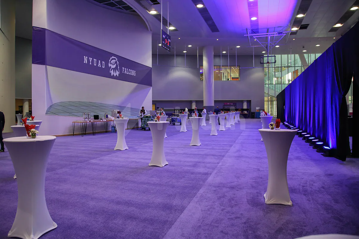 Ballroom at NYU Abu Dhabi Athletic Field featuring purple carpet, white cocktail tables, and a purple NYUAD Falcons