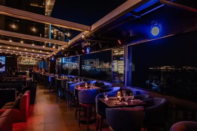 Rooftop terrace at Flooka Restaurant Dubai with dark blue chairs, wooden tables, and a night view of