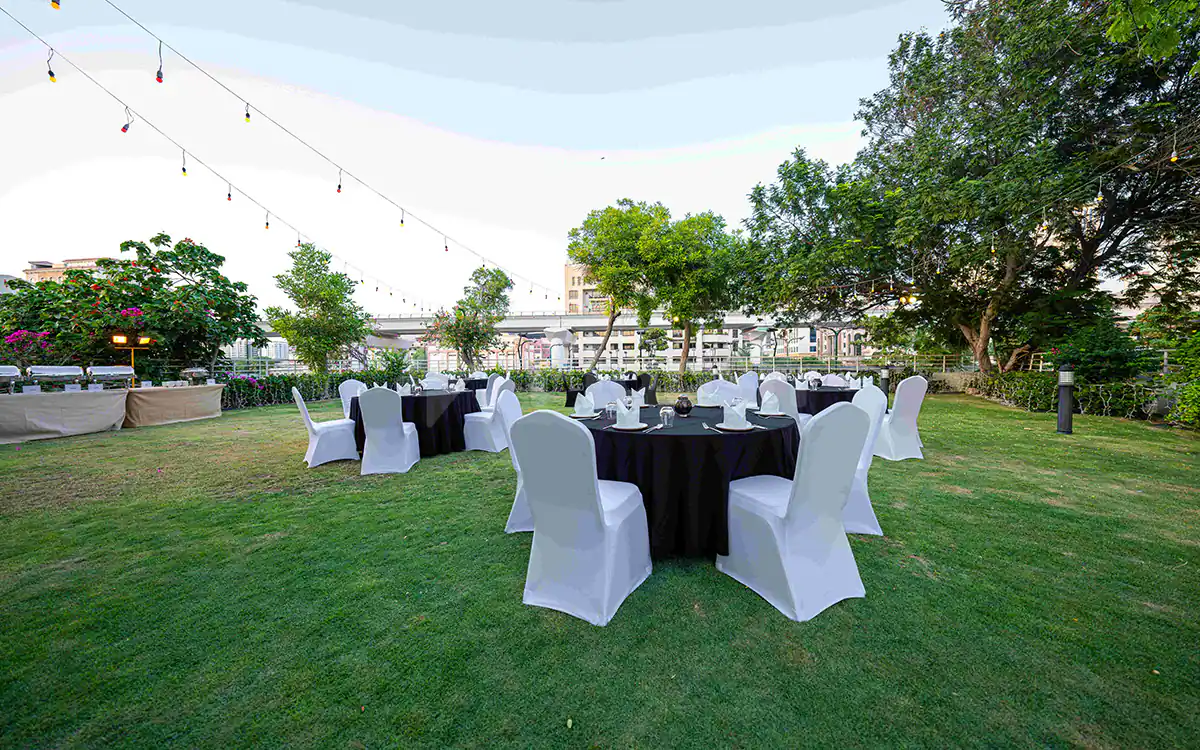 Terrace at Ashas Restaurant Dubai featuring a green lawn with round tables, white chair covers, and string lights