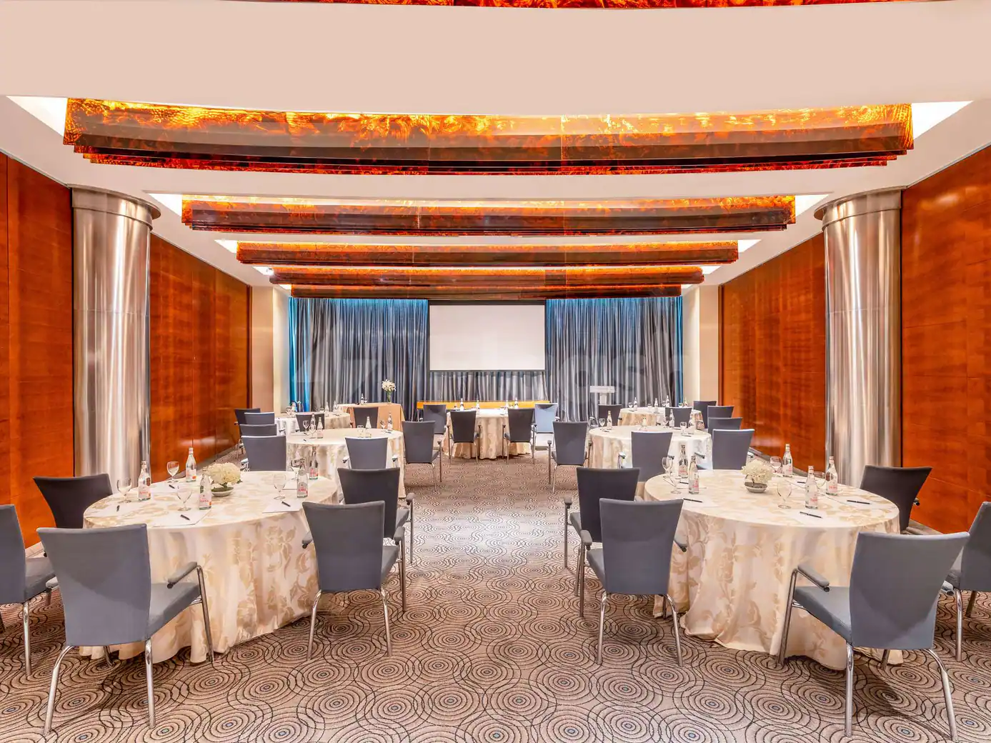 Meeting room at Movenpick Hotel AlKhobar Dammam with round tables, grey chairs, patterned carpet, wooden walls, and amber
