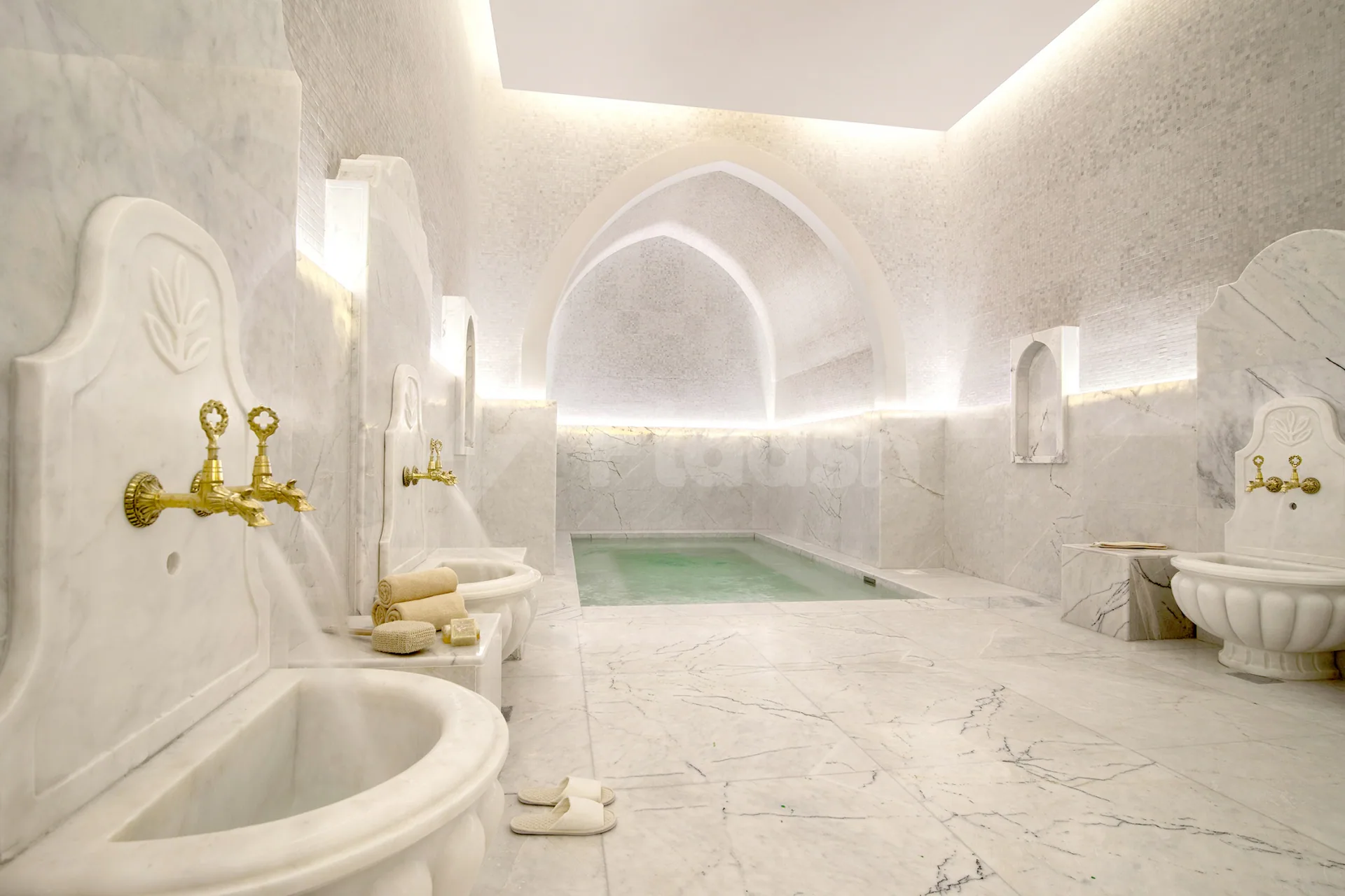 Hammam at Cristal Amaken Hotel Riyadh featuring white marble walls, a rectangular green-tinted pool, and ornate marble sinks