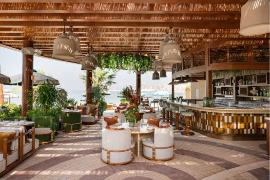 Rooftop terrace at Baoli Restaurant Dubai featuring a thatched roof, wooden pillars, hanging pendant lights, and an ocean