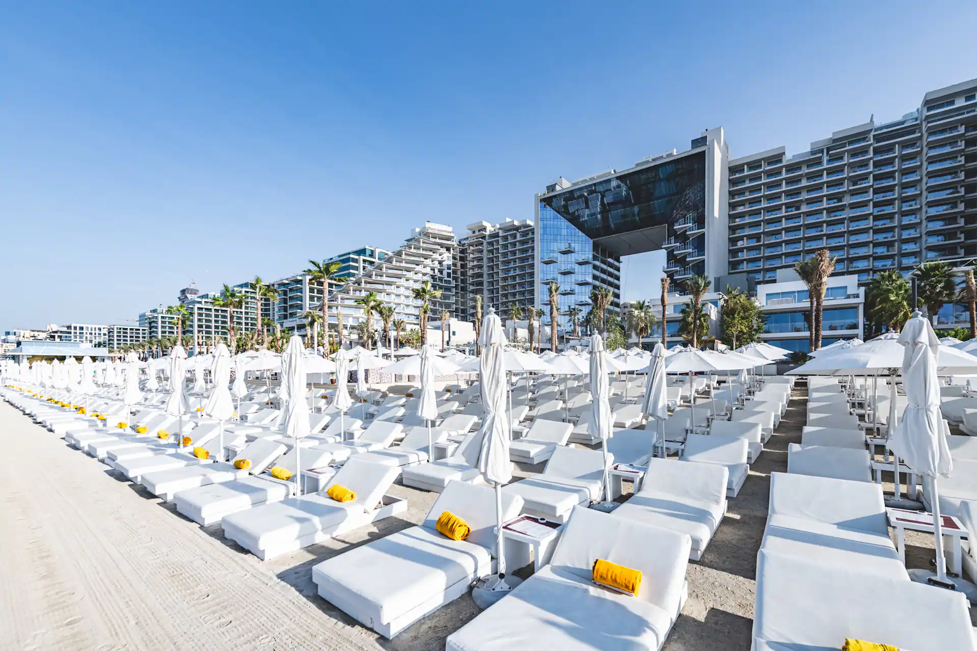 Beach By Five Beach Party Dubai outdoor seating area with white sun loungers, yellow towels, and modern high-rise