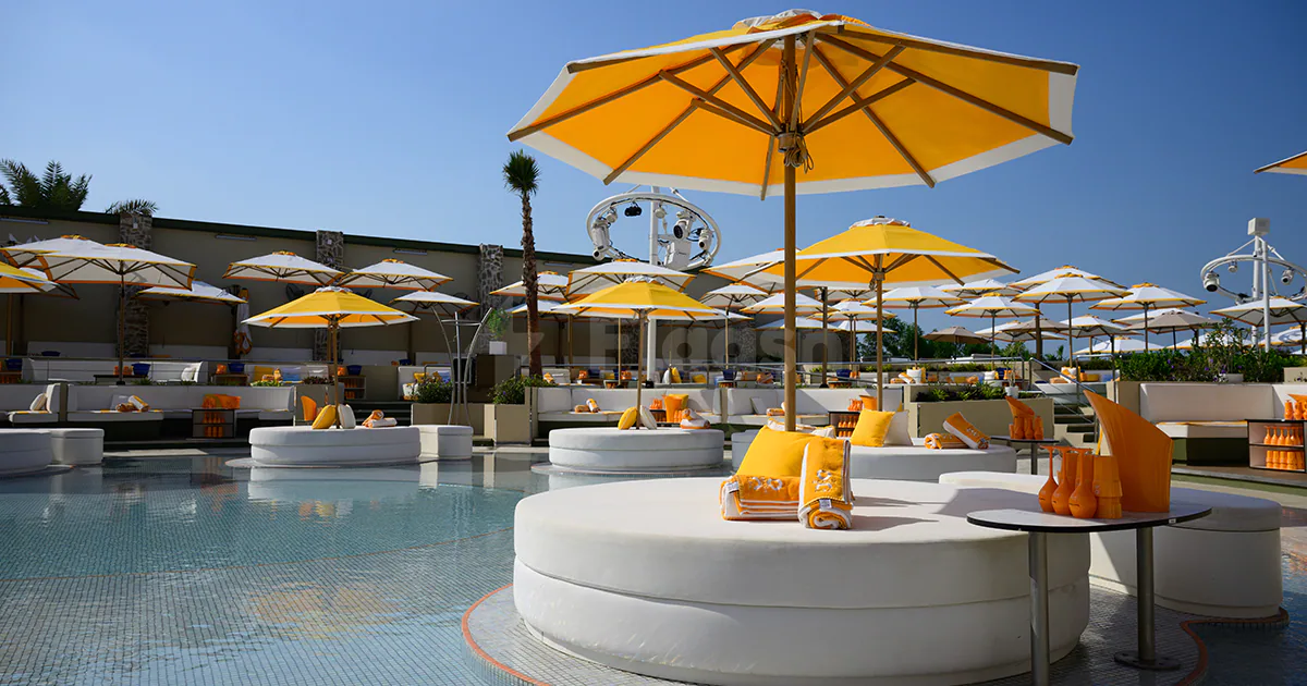 Swimming pool at O Beach Dubai featuring white circular lounge seating and yellow umbrellas under a clear blue