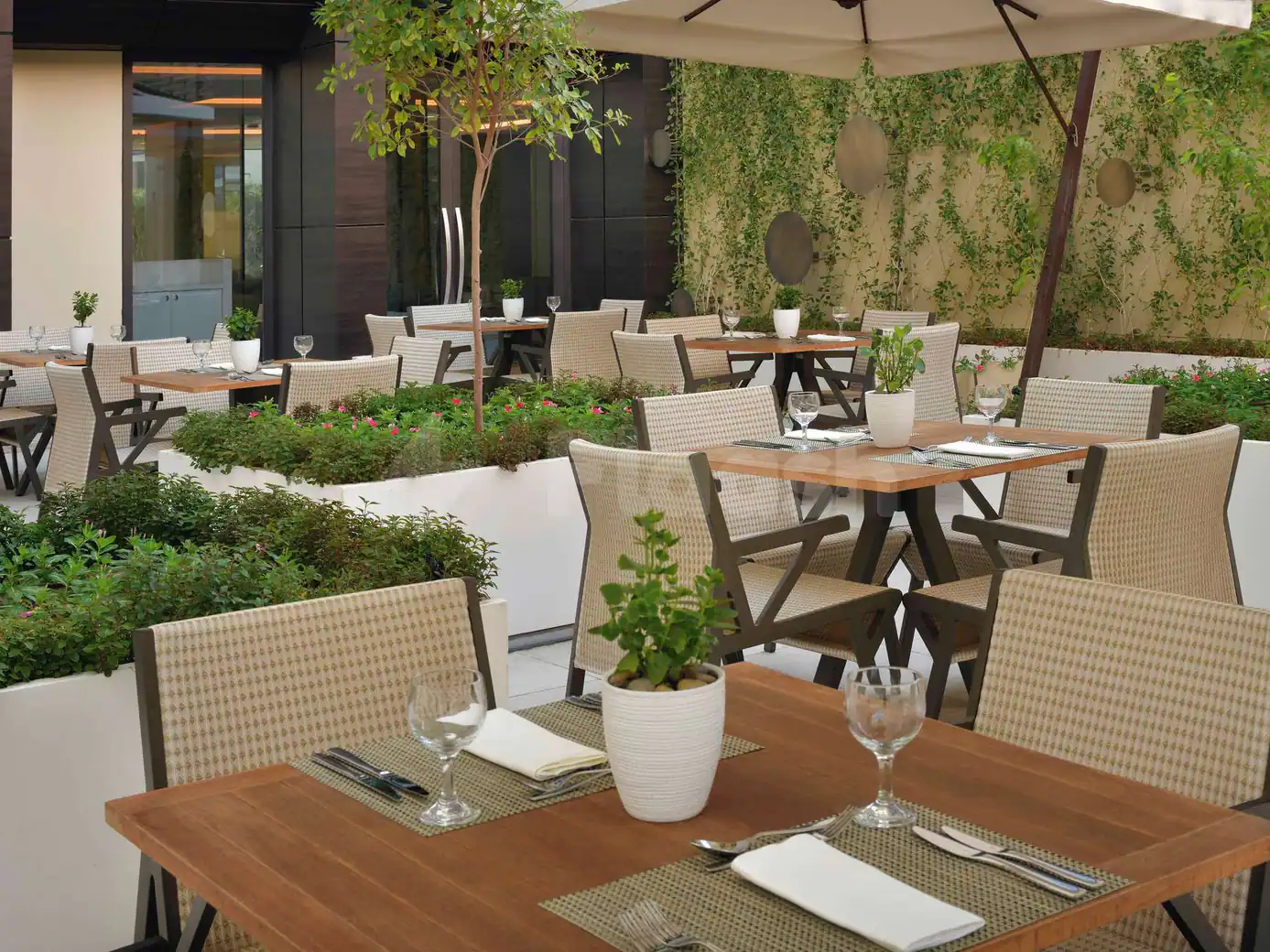 Rooftop terrace at Rasoi By Vineet Jeddah featuring wooden tables with woven chairs, raised garden beds