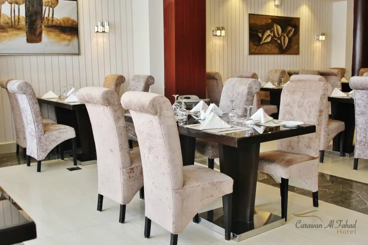 Restaurant at Carawan Al Fahad Hotel Riyadh featuring black wooden tables with white napkins and pink velvet chairs