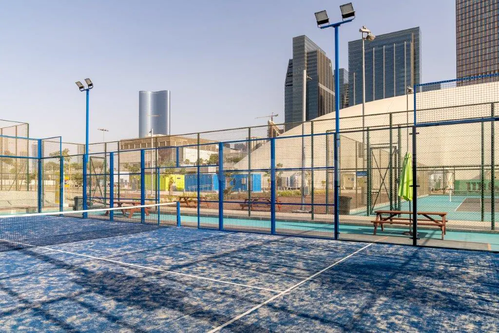 Blue tennis court at Active Al Maryah Island Sports & Recreation in Abu Dhabi with netted enclosure and floodlights