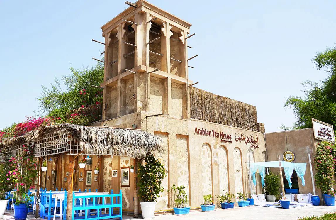 Sand-coloured adobe building with traditional wind tower and thatched roof canopy at Arabian Tea House Restaurant & Cafe