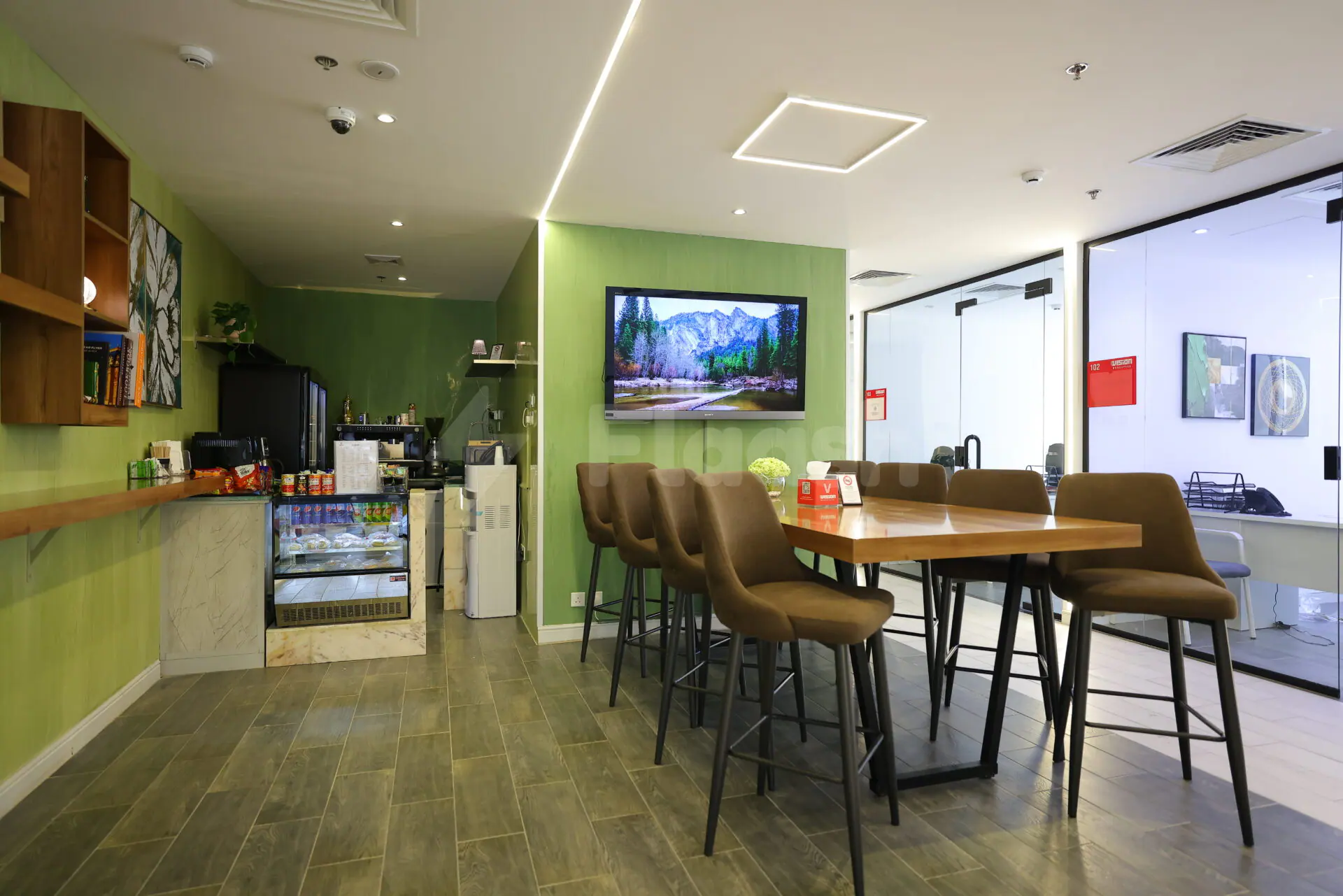 Restaurant at Vision Work Space Jeddah featuring a wooden table with brown stools, green accent wall, and mounted