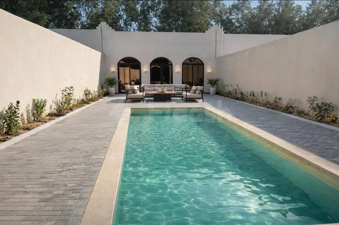 Rectangular swimming pool at Hdb Sahafa in Riyadh, flanked by paved walkways and a white stucco wall