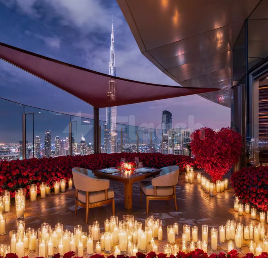 Rooftop terrace at CÉ LA VI Dubai with wooden table, two beige chairs, red rose arrangements, and Burj
