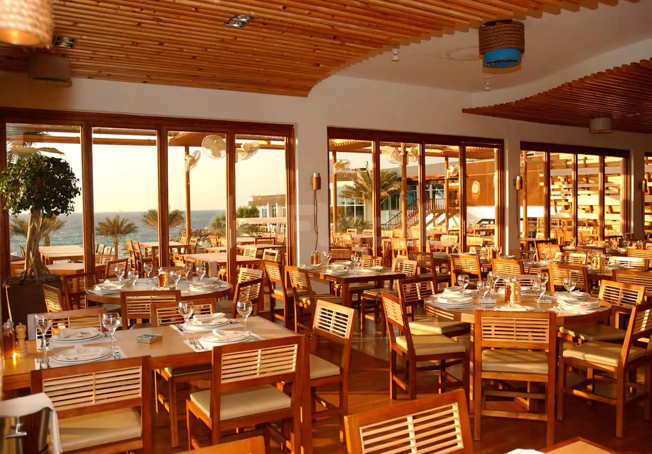 Flooka Restaurant Dubai dining area with wooden ceiling and large windows overlooking the ocean and palm trees