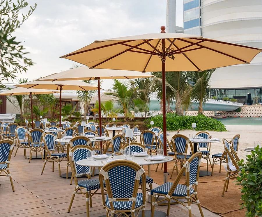 Terrace at Lucia's Mare Restaurant Dubai featuring wooden decking, beige patio umbrellas, and a view of palm trees
