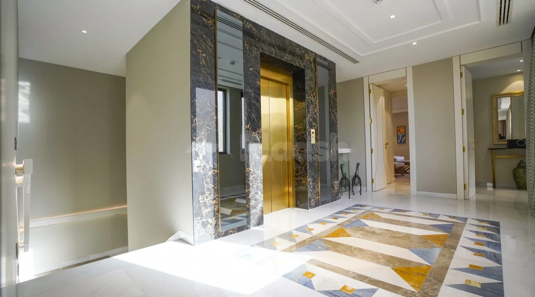 Entrance hall at Vivienda Hada Residences in Riyadh featuring a gold-door elevator framed by black marble with gold