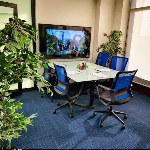 Boardroom at Basix Coworking Space Jeddah featuring a rectangular glass table, blue mesh chairs, and a wall-mounted TV