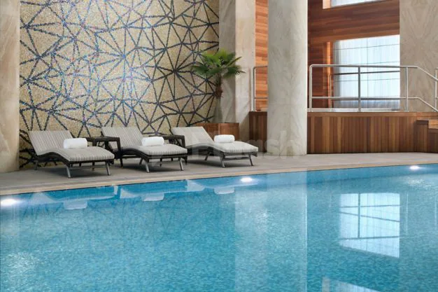 Indoor swimming pool at Marriott Executive Apartments Al Khobar featuring a geometric mosaic wall and stone pillars