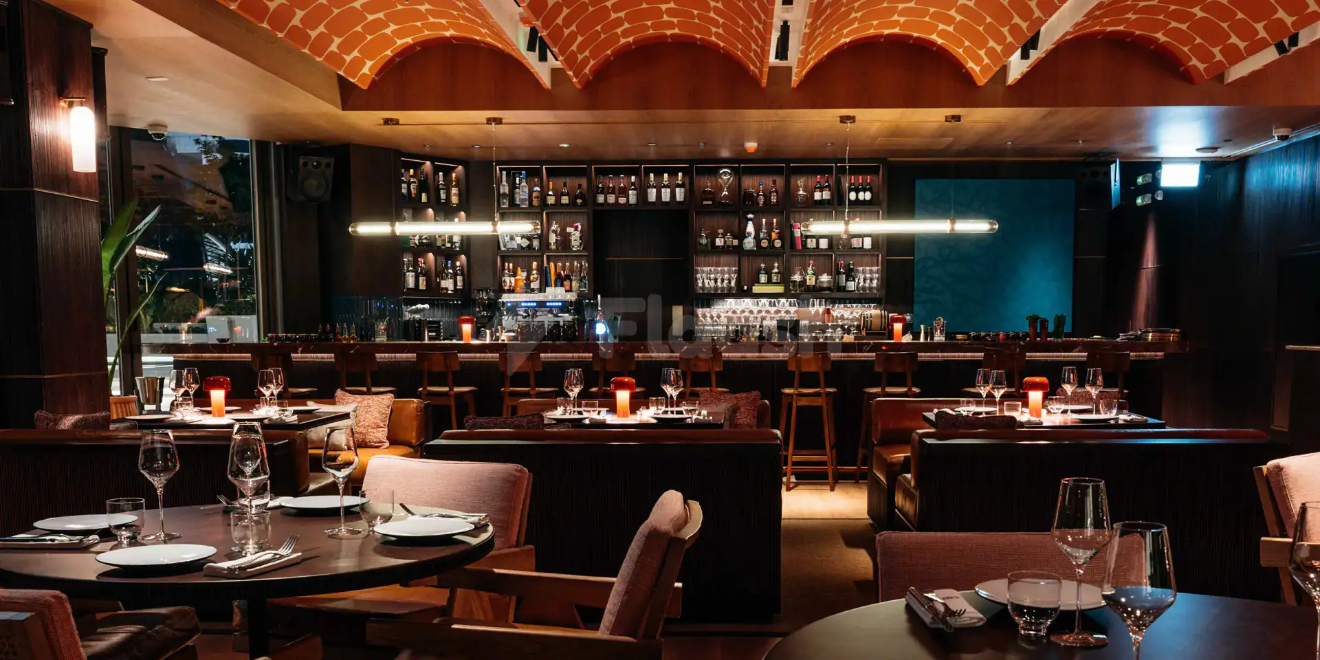 Restaurant interior at Chez Wam in Dubai featuring a red brick arched ceiling and a backlit bar