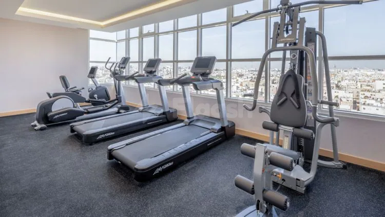 Gym at Residence Inn Dammam featuring treadmills and a multi-station machine with large windows overlooking the city