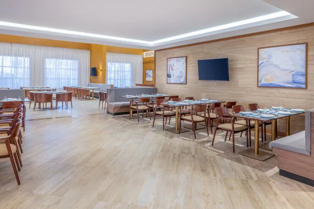 Restaurant at Residence Inn Dammam featuring set dining tables with blue tablecloths, wood-paneled walls, and large windows