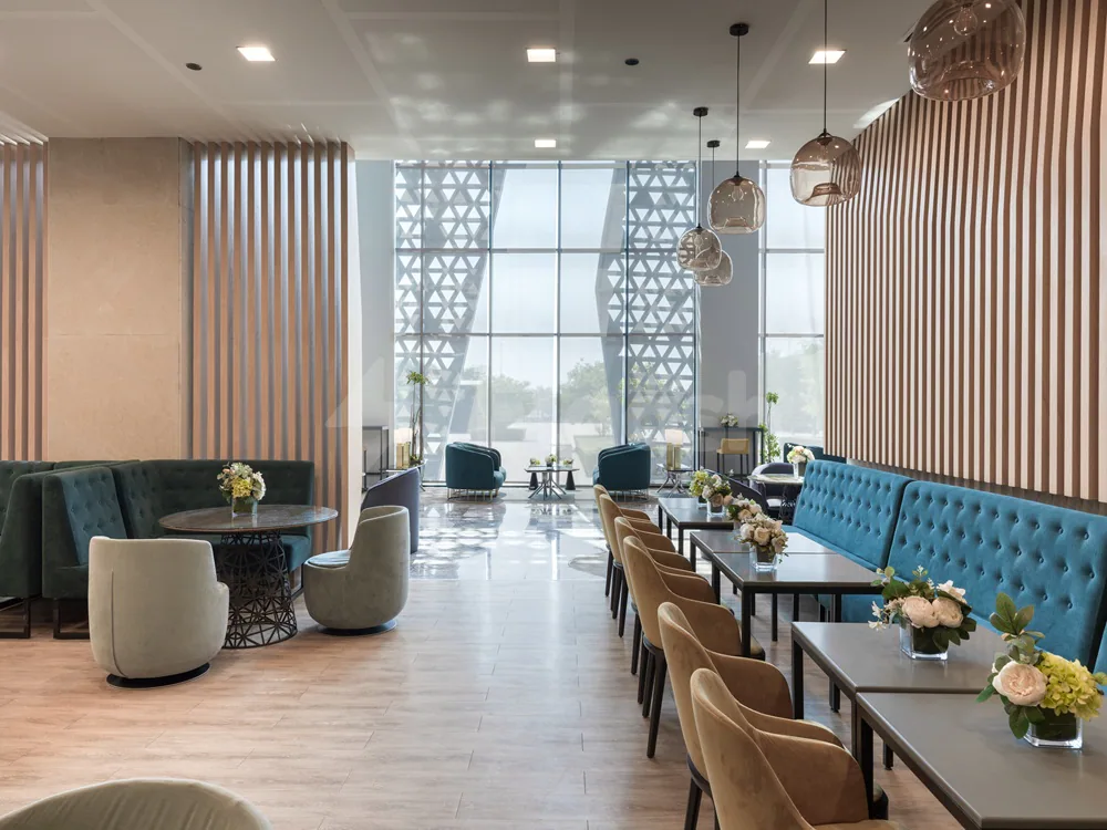 Restaurant at Dhahran International Exhibition Center in Dammam featuring teal tufted banquettes, beige upholstered chairs, and large geometric