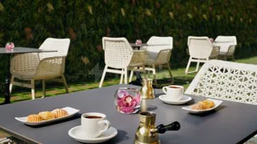 Rooftop terrace at Marriott Executive Apartments Al Khobar with white wicker chairs, dark grey table, brass cezve