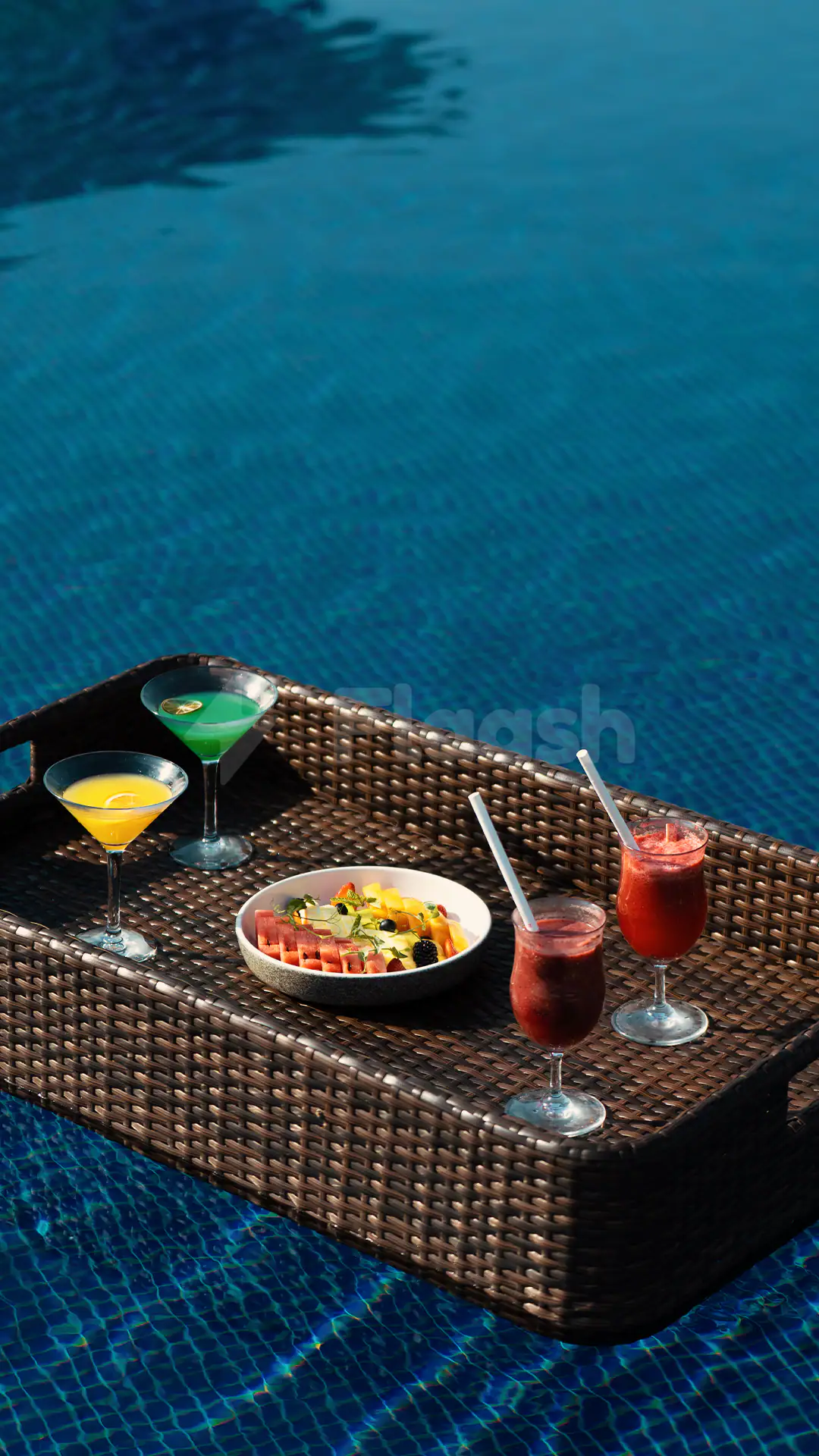 Swimming pool at Al Zorah Golf Club in Ajman with a woven tray holding cocktails and fruit salad