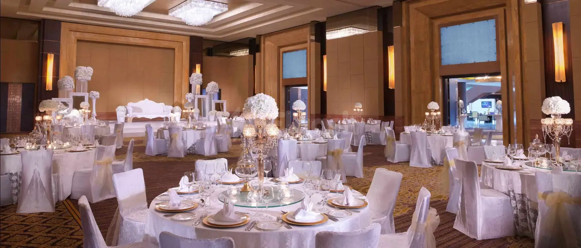 Ballroom at Namak Restaurant Abu Dhabi set with round tables, white chair covers, gold sashes, and crystal candelabras