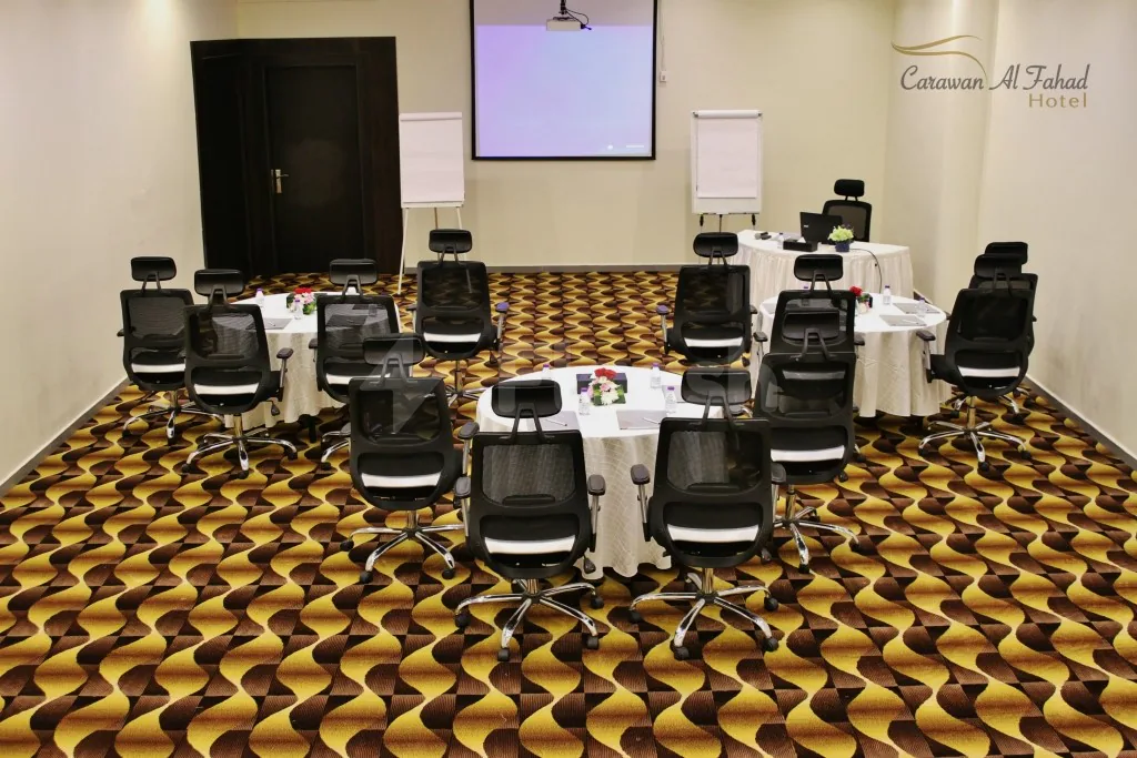 Meeting room at Carawan Al Fahad Hotel Riyadh with round tables, black mesh chairs, and a patterned carpet