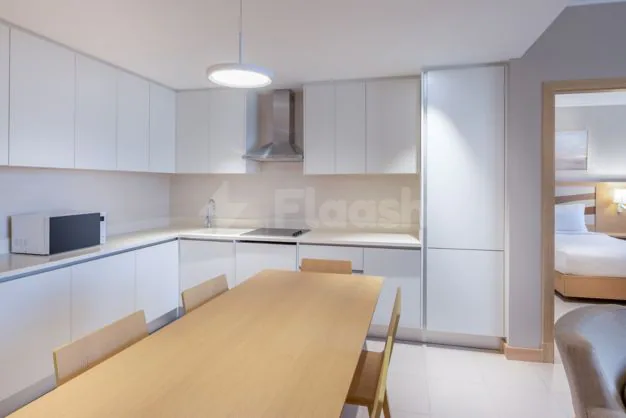 Modern kitchen at Residence Inn Dammam featuring white cabinets, a wooden dining table, and an open-plan layout