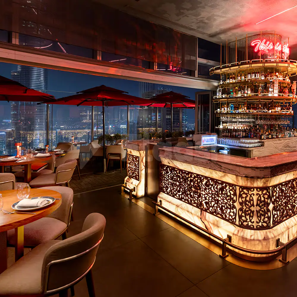 Bar counter at CÉ LA VI Dubai featuring a backlit ornate metal screen and neon sign overlooking