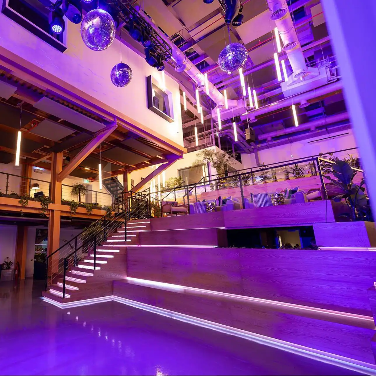Ballroom at Jax 01 Riyadh featuring tiered wooden seating, disco balls, and suspended linear lights under an exposed