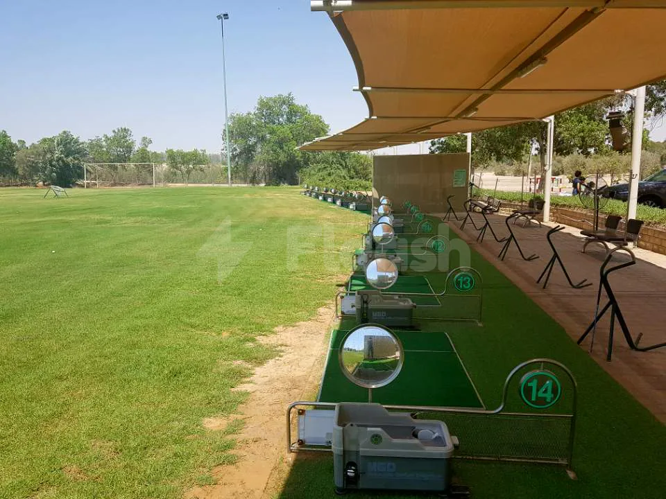 Outdoor driving range at Al Ghazal Golf Club in Abu Dhabi with numbered stations and circular mirrors