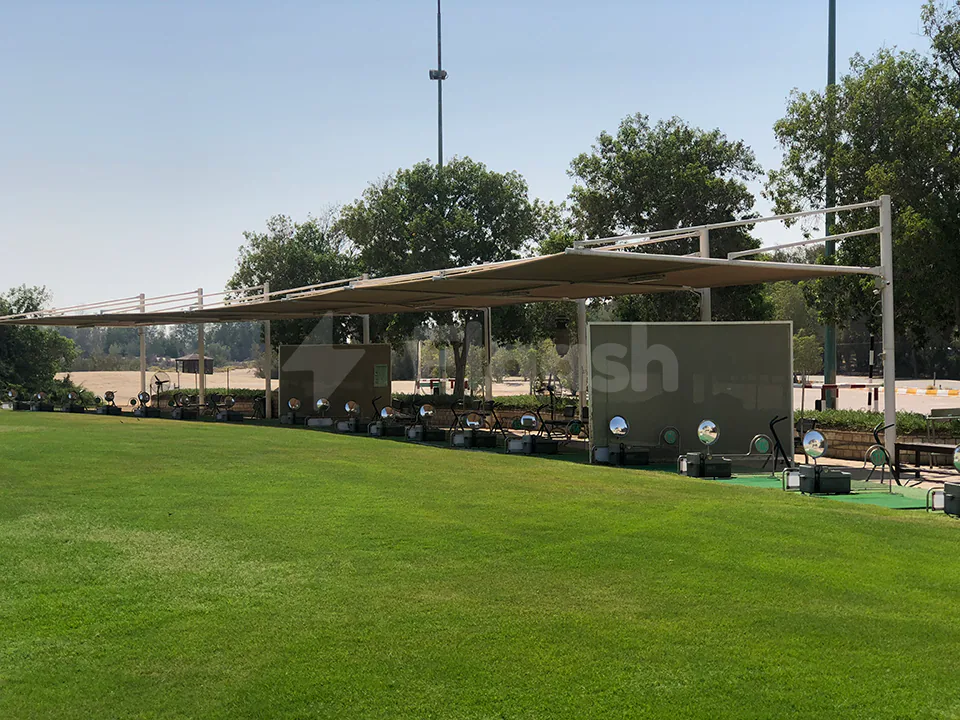 Al Ghazal Golf Club Abu Dhabi outdoor terrace with metal canopy, green lawn, and golf practice stations under