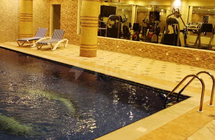Indoor swimming pool at Carawan Al Fahad Hotel Riyadh with tiled edge, lounge chairs, and mirrored wall reflecting