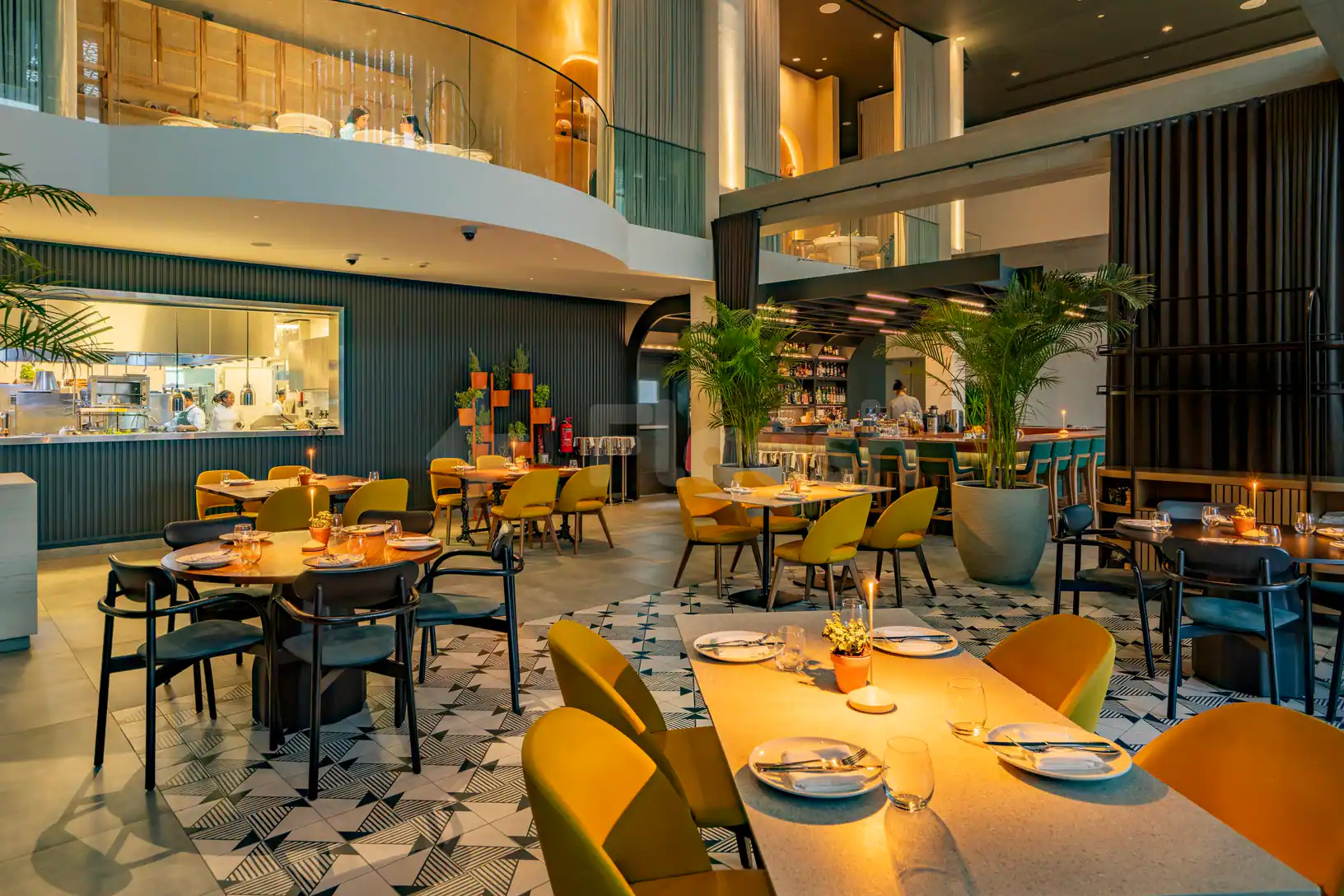 Taparelle Restaurant in Abu Dhabi features a modern multi-level interior with an open kitchen and large potted palms