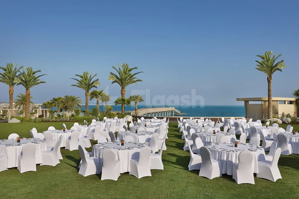 Outdoor wedding reception setup at Waldorf Astoria Doha Lusail, featuring white-draped tables under palm trees by the sea