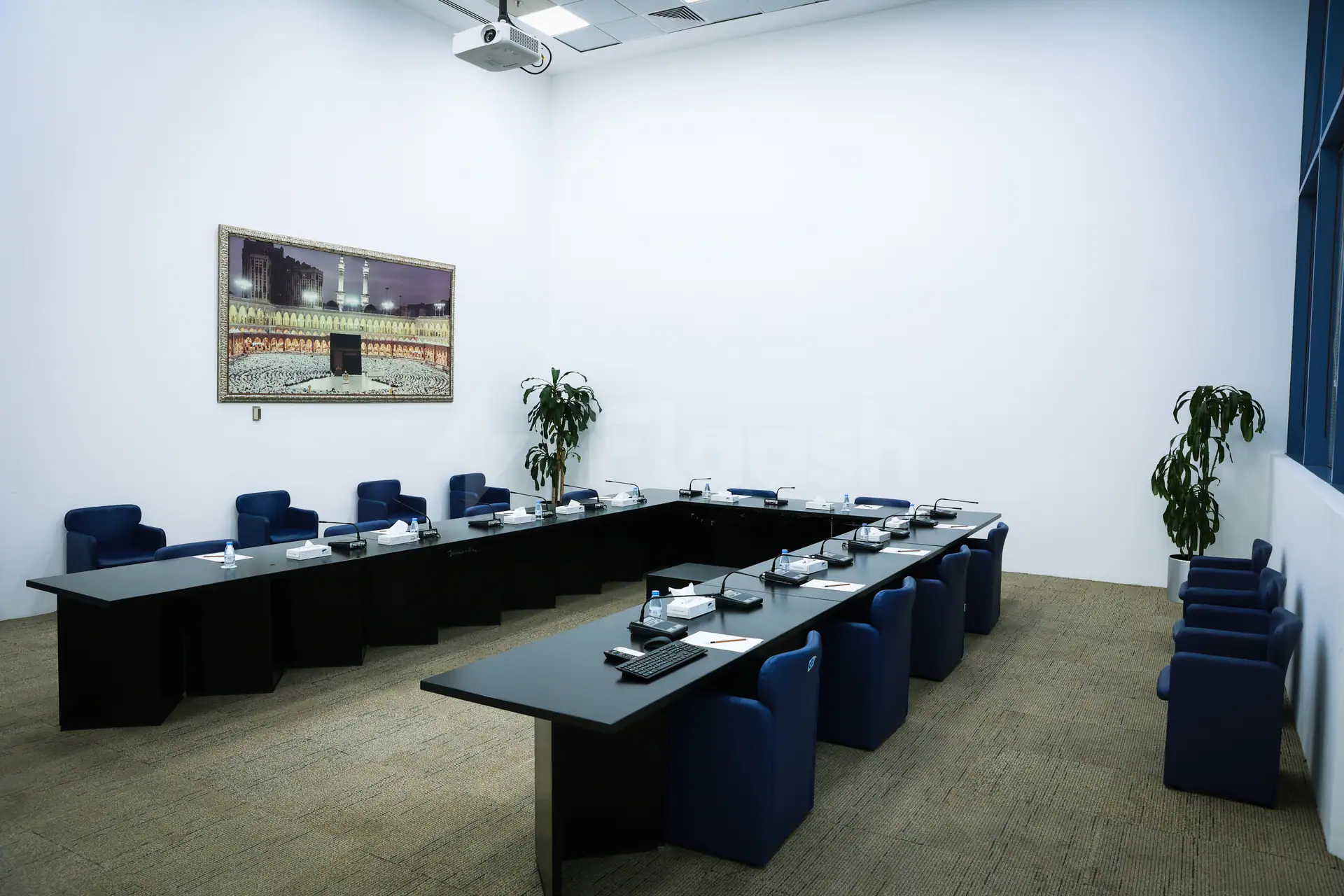 Boardroom at Jeddah International Exhibition & Convention Center featuring a U-shaped black table, blue armchairs, and framed wall art