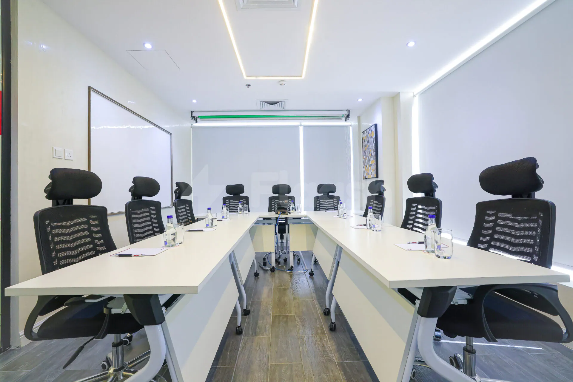Boardroom at Vision Work Space Jeddah featuring a long white table, black mesh chairs, wooden flooring, and ceiling
