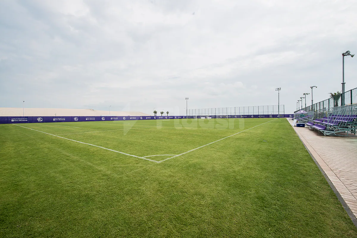 Green artificial turf field at NYU Abu Dhabi Athletic Field in Abu Dhabi with purple spectator seating