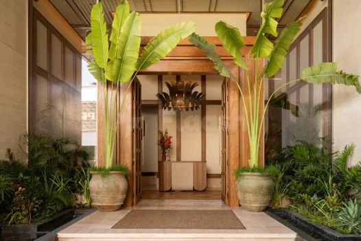 Entrance hall at Baoli Restaurant Dubai featuring wooden double doors flanked by large potted banana plants in stone