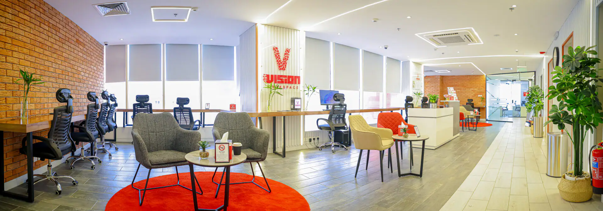 Entrance hall of Vision Work Space Jeddah featuring a white reception desk, exposed brick wall, and red circular