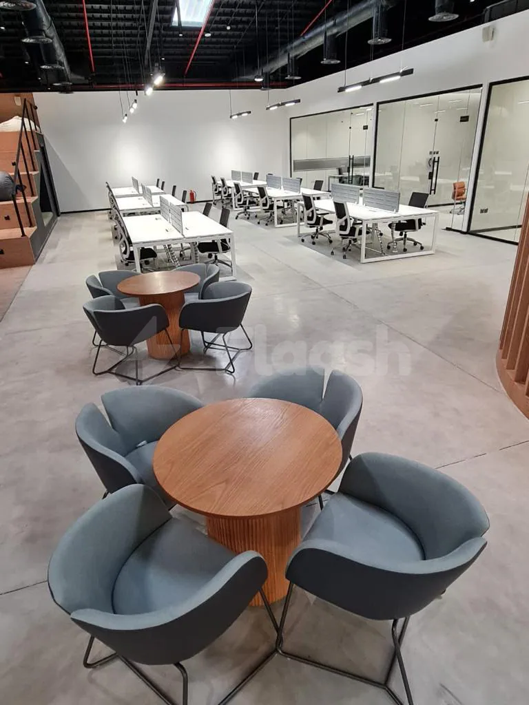 Meeting room at Jax 01 Riyadh featuring round wooden tables with grey upholstered chairs and glass partition walls