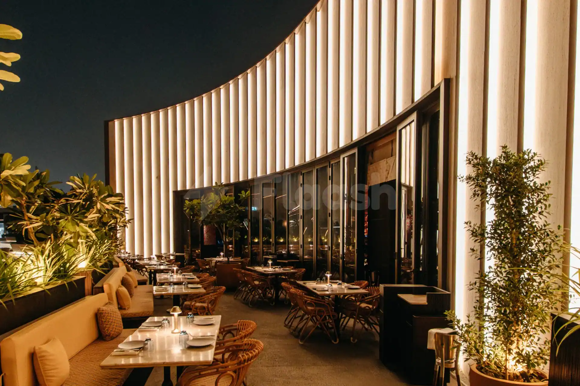 Rooftop terrace at Chez Wam in Dubai featuring a curved illuminated wall and potted plants alongside set dining